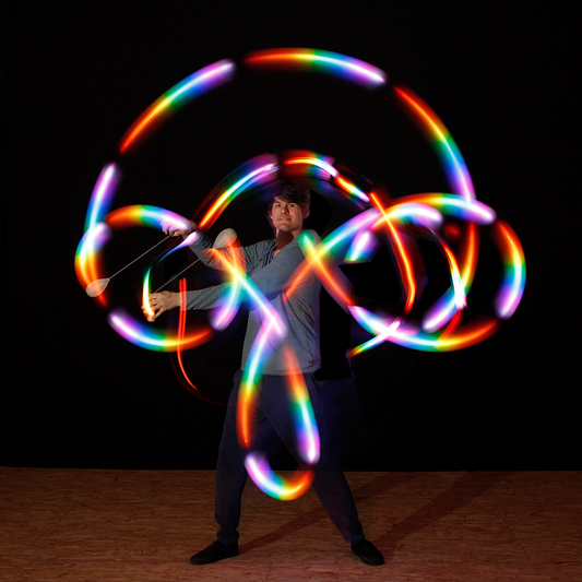 a performer spinning flowtoys LED podpoi with capsule handles, creating rainbow light trails