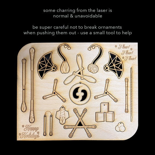 flowtoys wood lasercut holiday ornaments featuring podpoi, coral poi, vision clubs, trikon dragonstaff, juggling balls and boxes, leviwand, contact saber, dart, chucks and doodle grip fans. Warning text on being careful when removing.