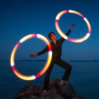 Francesca spinning flowtoys LED podpoi with red, yellow, orange and white light trails while standing on rocks at the ocean