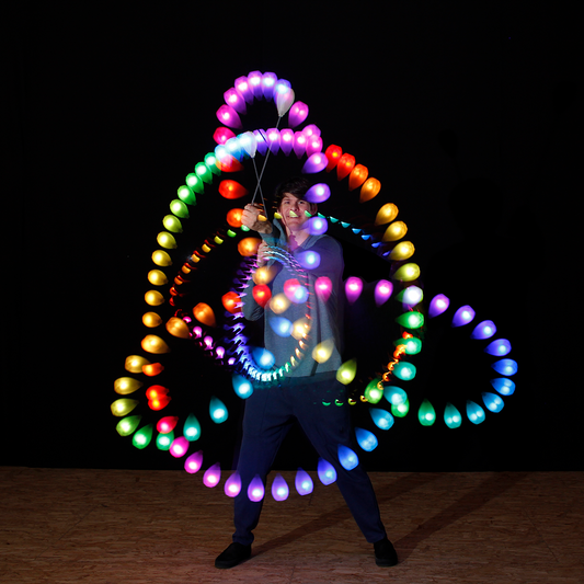 a performer spinning flowtoys LED podpoi with capsule handles, creating rainbow strobe light trails